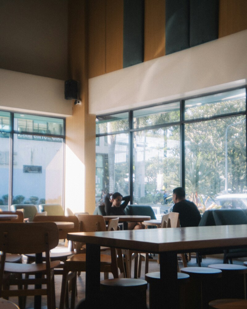 Interiørbilde fra en ikke navngitt coffeshop, to personer sitter ved et bord og prater.