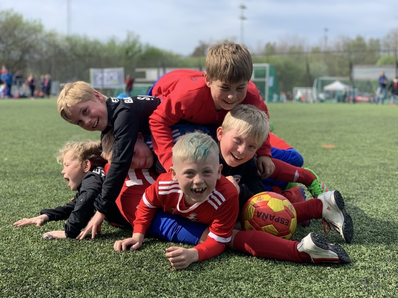 En klynge med fotballgutter, seks gutter som smiler og ler og har det gøy med fotball.